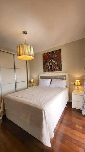 Ein Schlafzimmer mit Bett, Nachttischlampen, einem Gemälde an der Wand und einem Kleiderschrank.