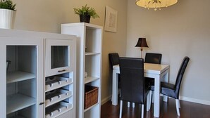 Un comedor con mesa, sillas, una araña y muebles blancos con estantes abiertos.
