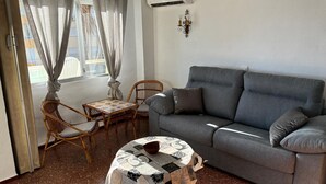A living room with a grey sofa, two wicker chairs, a small round table with a patterned tablecloth, and a window with curtains. - Terrasol Sobre EL MAR Habana 4 (Algarrobo)