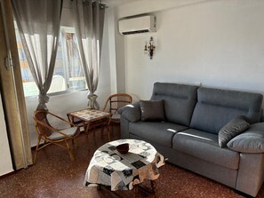 A living room with a grey sofa, two wicker chairs, a small round table with a patterned tablecloth, and a window with curtains. - Terrasol Sobre EL MAR Habana 4 (Algarrobo)