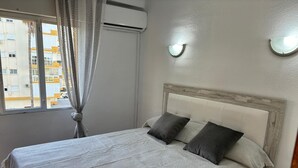 A bedroom with a bed, a window with curtains, an air conditioning unit, and a wall-mounted light fixture. - Terrasol Sobre EL MAR Habana 4 (Algarrobo)