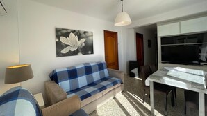 A living room with a sofa, a dining table, a TV, and a ceiling light. - Terrasol SAN Gerardo 2-1-3 Frontal AL MAR (Velez-Malaga)