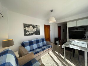 Ein Wohnzimmer mit einer Couch, einem Esstisch, einem Fernseher und einer Deckenleuchte.