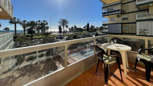 A balcony with a table and chairs, overlooking a beach and palm trees. - Terrasol SAN Gerardo 2-1-3 Frontal AL MAR (Velez-Malaga)