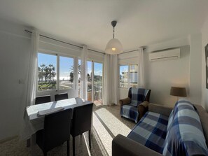 Ein Zimmer mit Esstisch, Stühlen, einer Couch und Blick auf Palmen und Gebäude.