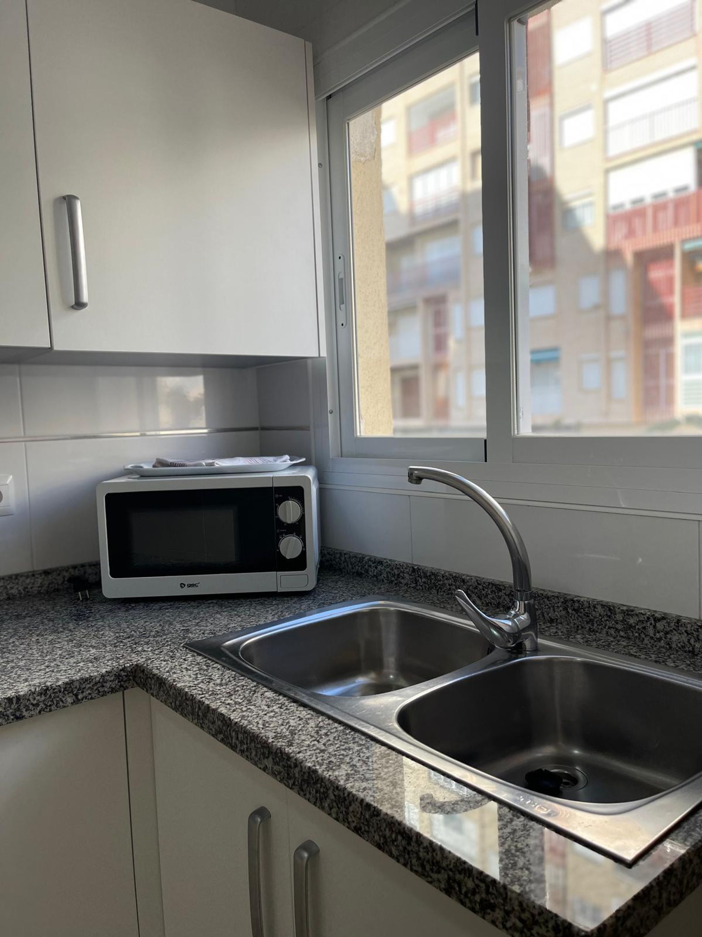 A kitchen with a microwave, double sink, and cabinets.