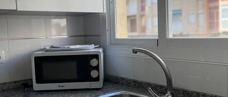 A kitchen with a microwave, double sink, and cabinets.