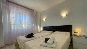 A hotel room with two beds, a window with sheer curtains, a nightstand with a lamp, and a wall-mounted light. - Terrasol SAN Gerardo 2-1-3 Frontal AL MAR (Velez-Malaga)