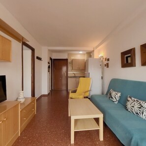 A living room with a sofa, a coffee table, a TV, and a kitchen in the background. - Terrasol Plazamar 2-6 (Velez-Malaga)