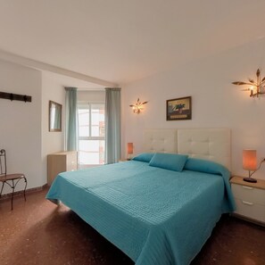 A bedroom with a bed, a nightstand, a chair, a window with curtains, and wall-mounted lights. - Terrasol Plazamar 2-6 (Velez-Malaga)