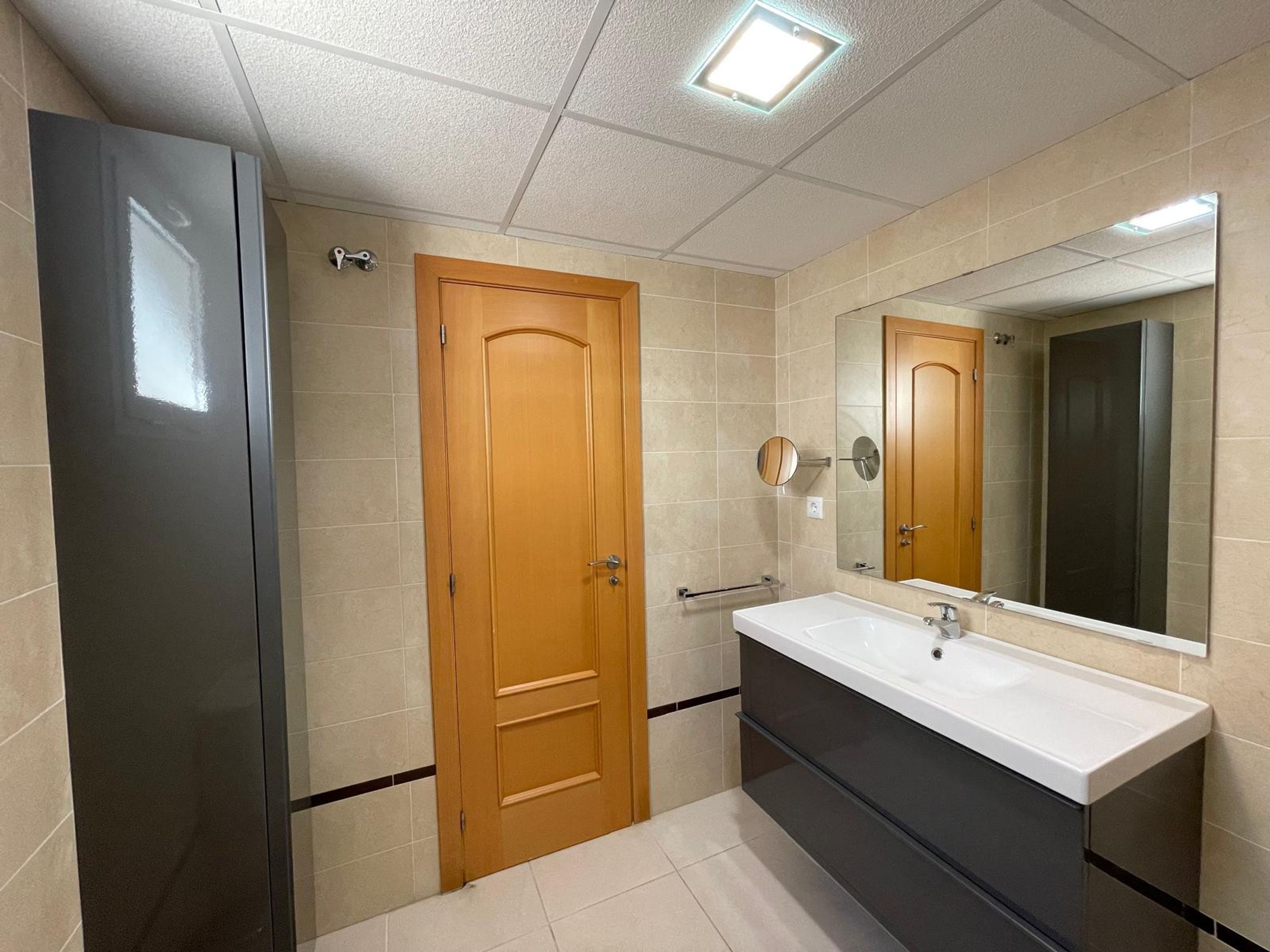 A bathroom with a wooden door, a white sink, a mirror, and a shower enclosure.