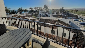 A balcony with a table and chairs, overlooking a courtyard with palm trees and buildings. - Terrasol Puerto Blanco 4d-10 (Velez-Malaga)