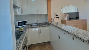 A compact kitchen with white cabinets, a microwave, a sink, and a countertop. - Terrasol Puerto Blanco 4d-10 (Velez-Malaga)