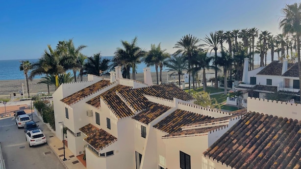 A coastal residential area with white buildings, tiled roofs, and palm trees. - Terrasol Puerto Blanco 4d-10 (Velez-Malaga)