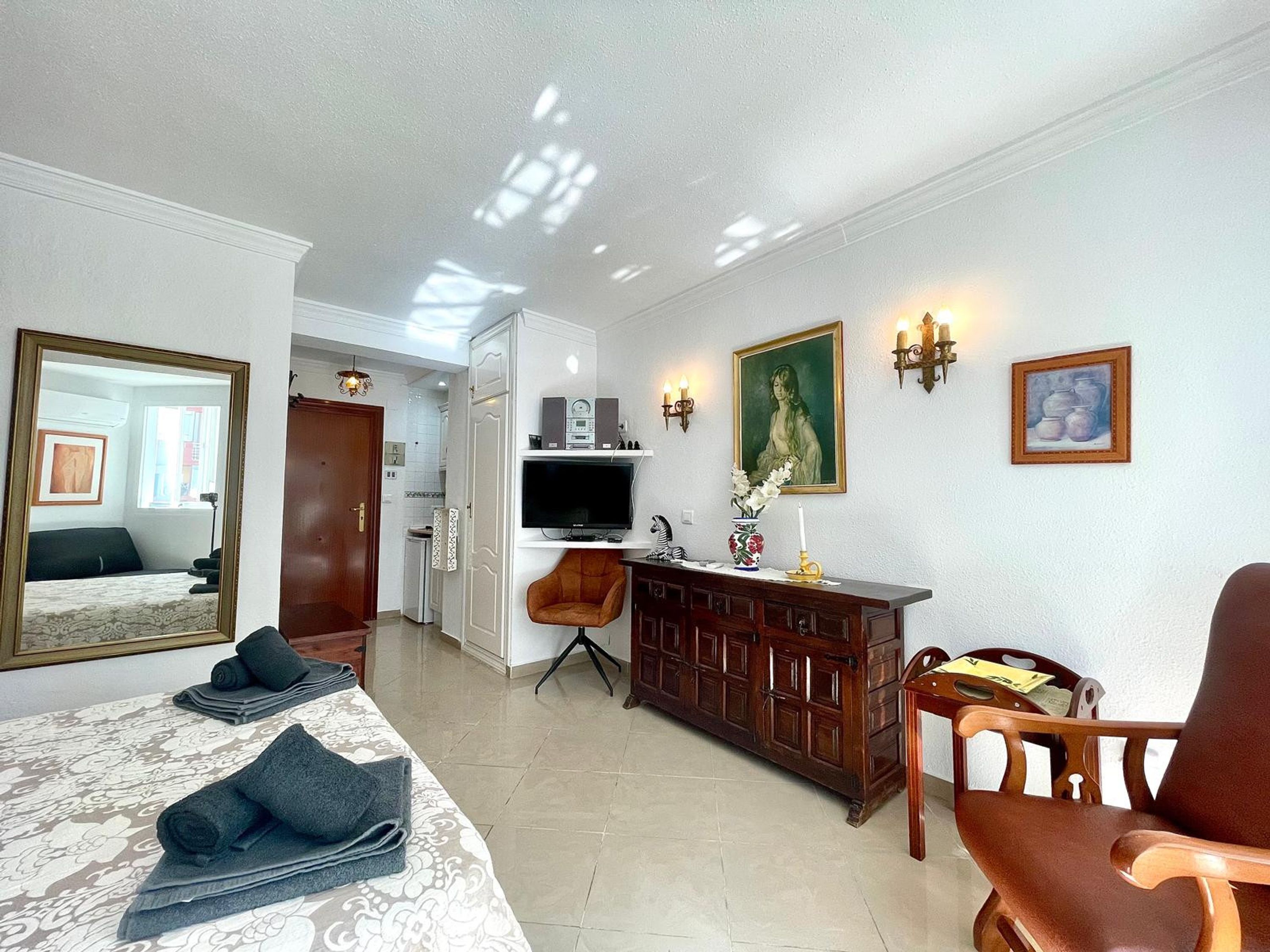 A hotel room with a bed, a TV, a wooden cabinet, a chair, and a mirror.