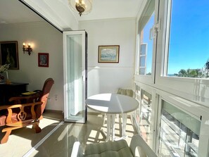 A room with a glass door leading to a balcony, a round table, a chair, and a small desk with a lamp. - Terrasol Plazamar 3-6 (Velez-Malaga)