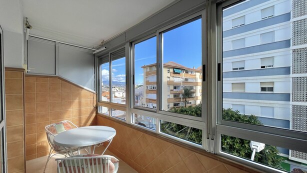 A balcony with a table and chairs, large windows, and a view of a residential building. - Terrasol Caracola 3 in Torre del Mar (Velez-Malaga)