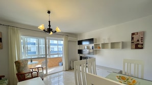A dining area with a table and chairs, a chandelier, a view of the outside balcony, and a wall-mounted shelf with decorative items. - Terrasol Caracola 3 in Torre del Mar (Velez-Malaga)