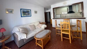 Un soggiorno con divano, tavolo in legno e angolo cottura con pensili e finestra.