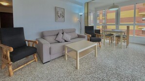 A modern living room with a sofa, two armchairs, a coffee table, and a dining area with a table and chairs. - Terrasol SAN Gerardo 2-2-2 Frontal AL MAR (Velez-Malaga)