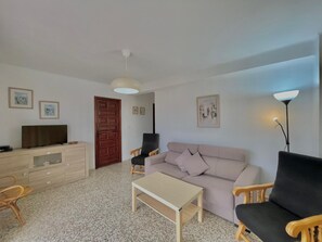 Un soggiorno con un divano, un tavolino, una televisione, un mobile in legno e una porta.