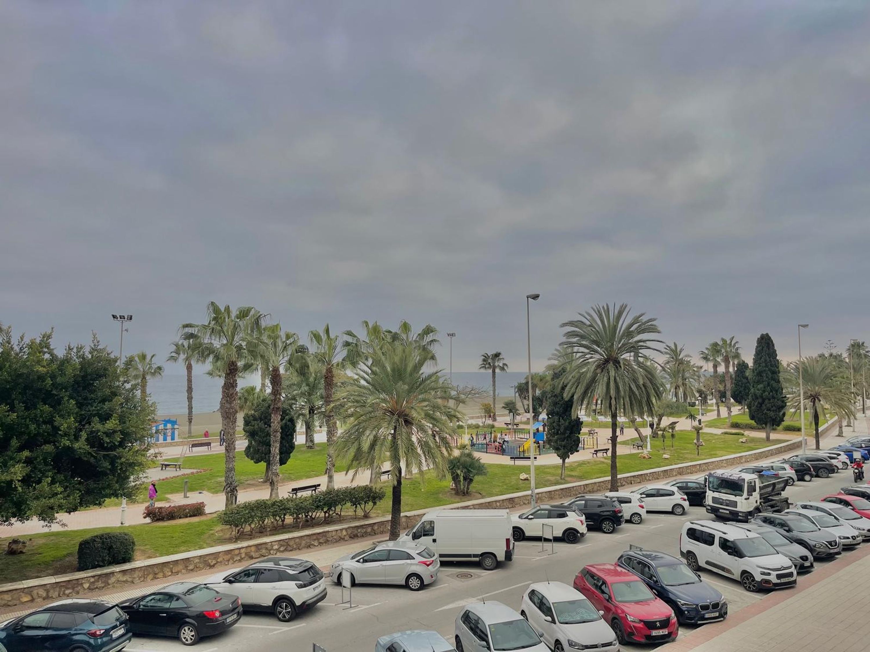 Un estacionamiento con varios autos y algunas personas caminando.