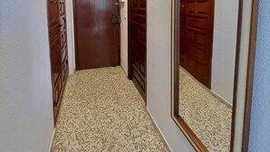 A hallway with a wooden door at the end, a mirror on the right wall, and a ceiling light. - Terrasol SAN Gerardo 2-2-2 Frontal AL MAR (Velez-Malaga)