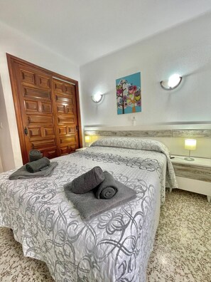 Una habitación de hotel con una cama, una puerta de madera, un cuadro y una mesita de noche.