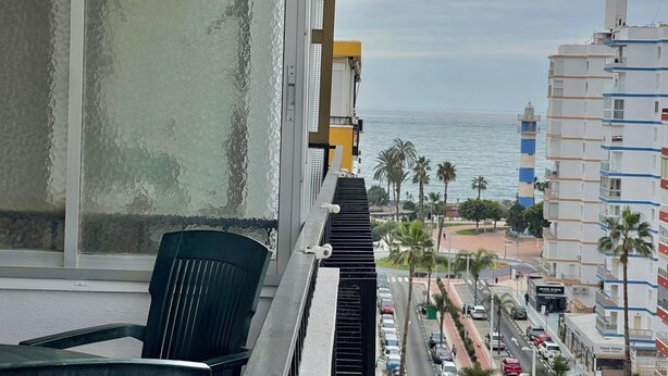 En balkon med udsigt over havet, en stol og en bygning med en blå og hvid facade.