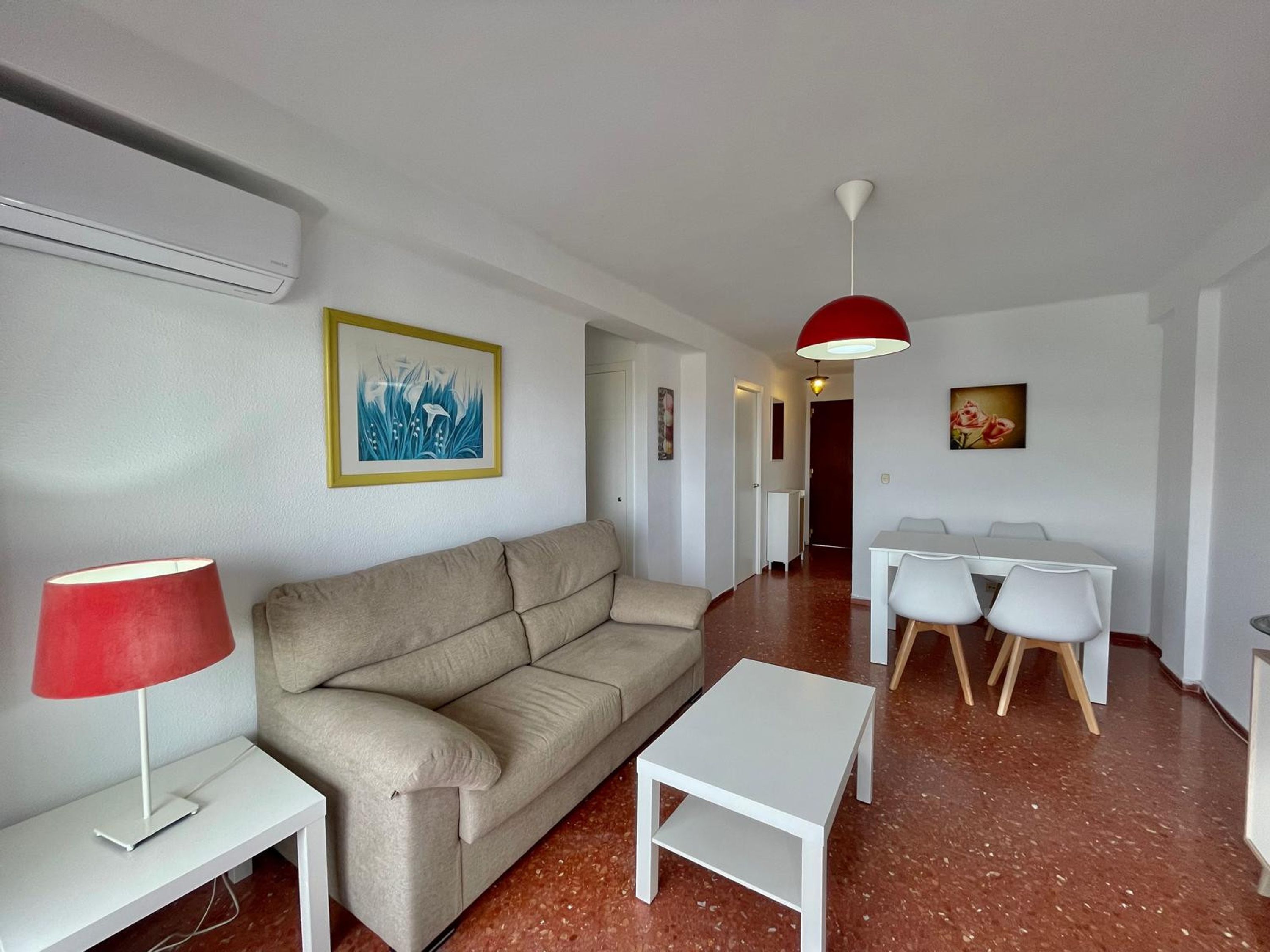 A modern living room with a sofa, a small table, a dining table with chairs, and artwork on the walls.