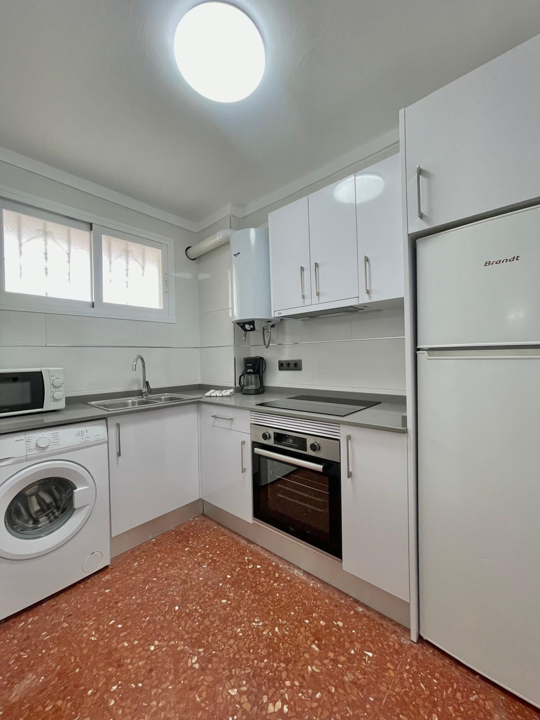 A compact kitchen with a washing machine, oven, and a Brandt refrigerator.