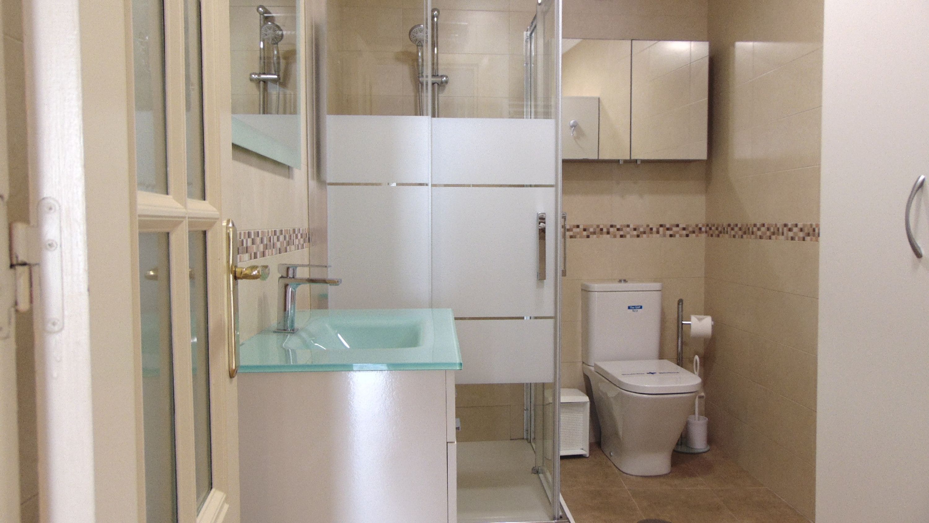 A bathroom with a glass sink, a toilet, and a shower.