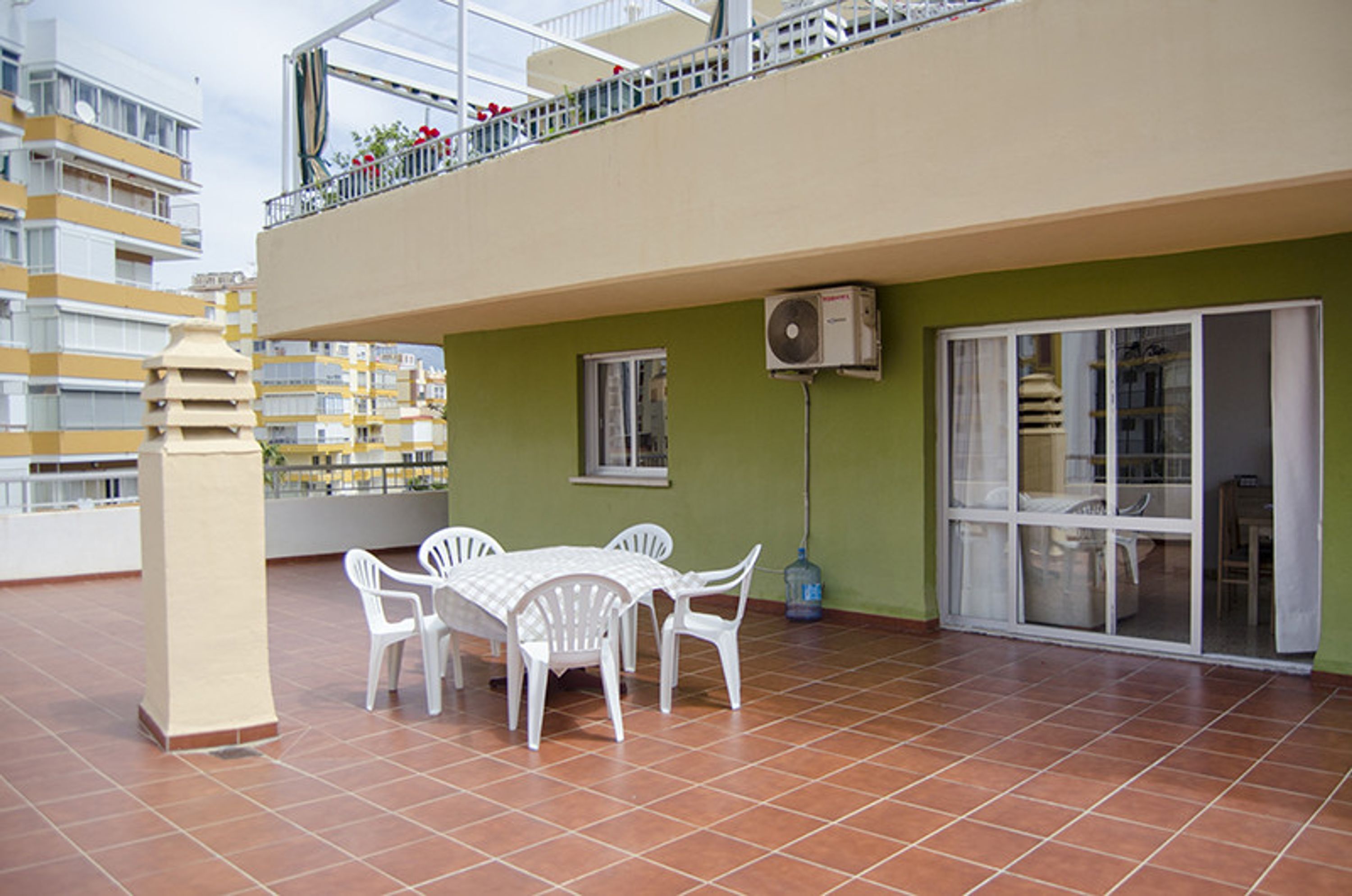 Una terraza con mesa y sillas, un dispensador de agua y vistas a un edificio con balcones.