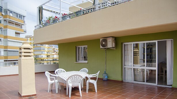 A terrace with a table and chairs, a water dispenser, and a view of a building with balconies. - Terrasol Caracola 5 in Torre del Mar (Velez-Malaga)
