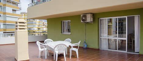 Una terraza con mesa y sillas, un dispensador de agua y vistas a un edificio con balcones.