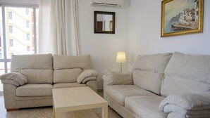 A living room with two sofas, a coffee table, a lamp, a painting, and a window with curtains. - Terrasol Caracola 5 in Torre del Mar (Velez-Malaga)