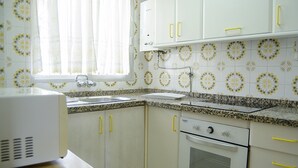 A kitchen with white cabinets, a stove, and a window with curtains. - Terrasol Caracola 5 in Torre del Mar (Velez-Malaga)