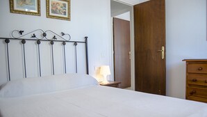 A bed with a metal headboard, a wooden dresser, and a door in a room with white walls. - Terrasol Caracola 5 in Torre del Mar (Velez-Malaga)