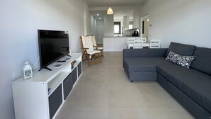A modern living room with a flat-screen TV, a sofa, a dining area, and a kitchen in the background. - Terrasol Almunia in Algarrobo (Algarrobo)