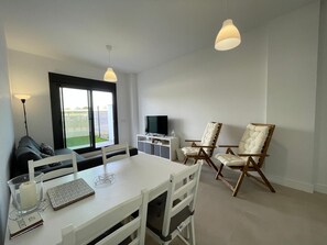 Ett modernt vardagsrum med ett vitt bord, två stolar, en tv och ett stort fönster.
