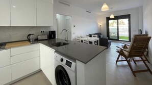 A modern kitchen with a built-in washing machine, a dining area with a table and chairs, and a large sliding glass door leading to an outdoor area. - Terrasol Almunia in Algarrobo (Algarrobo)