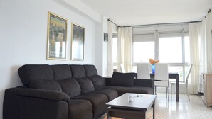 A modern living room with a dark sofa, a coffee table, and a dining area with chairs and a table. There are two framed pictures on the wall. - Terrasol SAN Gerardo 2-8-2 Frontal AL MAR (Velez-Malaga)