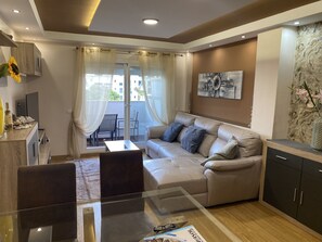 Ein modernes Wohnzimmer mit einem Glastisch, einer Couch, einem Esstisch und einer Küchenzeile.