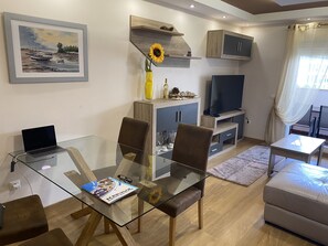 Ein modernes Wohnzimmer mit einem Glastisch, braunen Ledersesseln, einer Couch, einem Fernseher und einem Gemälde an der Wand.