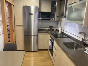 Eine kompakte Küche mit einem Edelstahl-Kühlschrank, einer Spüle und einer Arbeitsplatte mit Wasserkocher und Tassen.