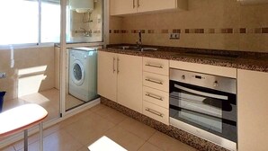 Cocina compacta con lavadora, horno y ventana con persianas.