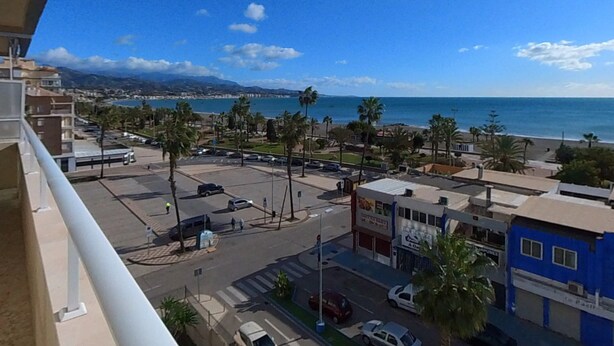 Un paisaje urbano costero con cielo despejado, edificios y una calle con coches estacionados.