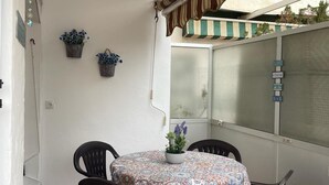 Un coin repas avec une table ronde, quatre chaises et une nappe à motifs. Deux plantes en pot sont accrochées au mur.