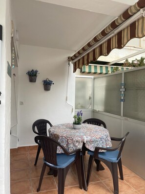 Ein Essbereich mit einem runden Tisch, vier Stühlen und einer Tischdecke mit Muster. An der Wand befinden sich zwei Blumentöpfe.