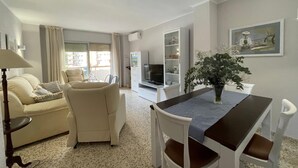 A living room with a sofa, armchair, dining table, and a TV. - Terrasol Estrella 2 in Torre del Mar (Velez-Malaga)